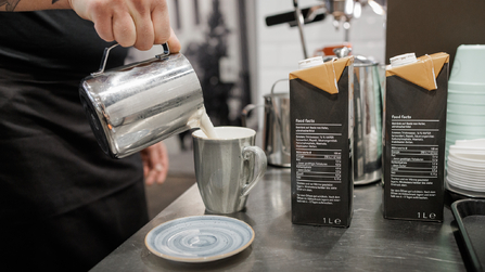 Milch wird in einen Metallbecher in einer Küche eingeschenkt.