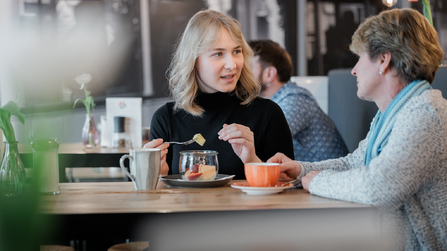 Zwei Frauen im Gespräch bei Kaffee und Frühstück in einem Restaurant.