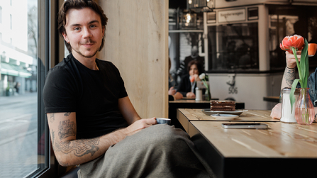 Junger Mann sitzt entspannt am Fenster eines Restaurants.