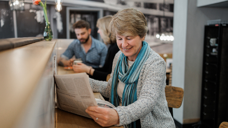 Frau liest Zeitung an einem Tisch in einem Restaurant.