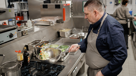 Koch bereitet in einer professionellen Küche Gemüse in einer Pfanne zu.
